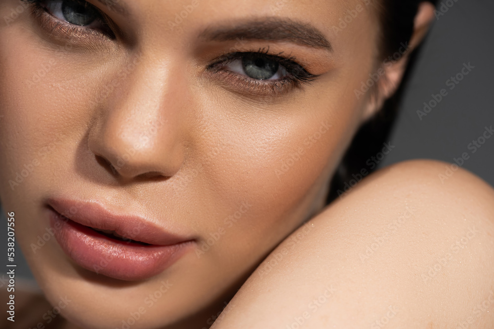 Close up view of young woman with visage looking at camera near shoulder isolated on grey. Close up view of young woman with visage looking at camera near shoulder isolated on grey.