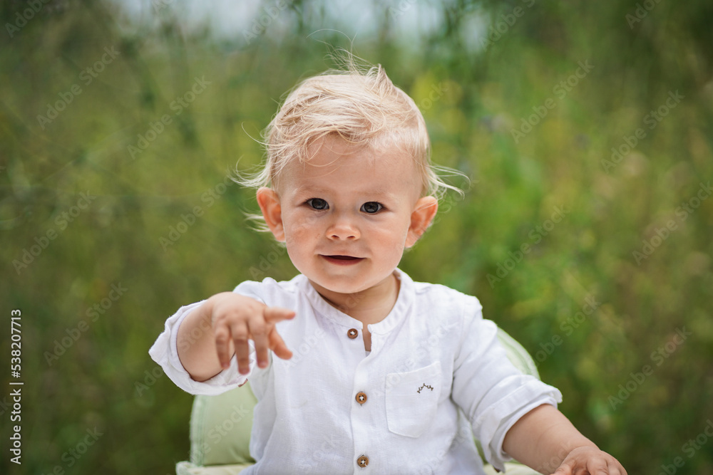 happy smiling one year old baby boy in chic festive summer clothes looking flirty into the camera outdoor in the garden with magical, idyllic & flowery green grass in the background happy smiling one year old baby boy in chic festive summer clothes looking flirty into the camera outdoor in the garden with magical, idyllic & flowery green grass in the background