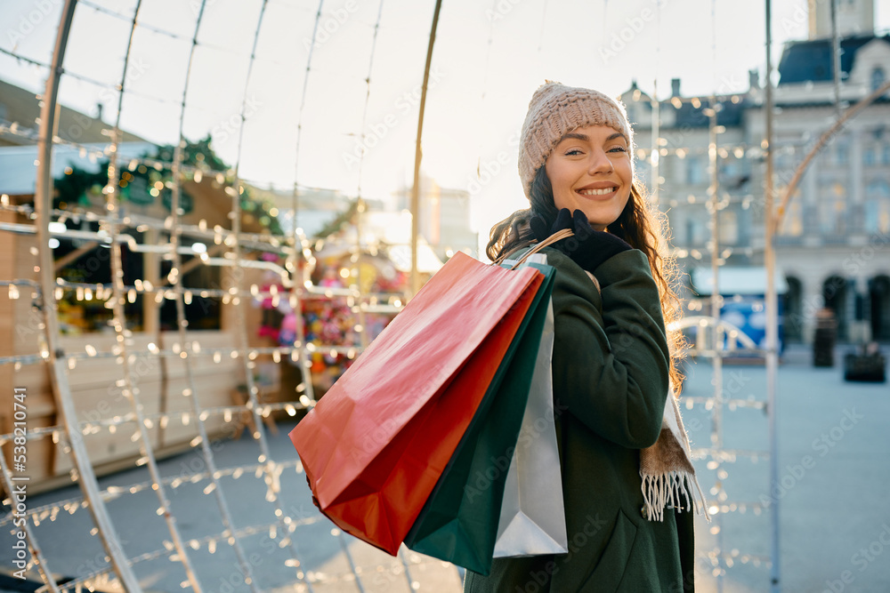 Happy woman enjoys in Christmas shopping during winter day and looking at camera.