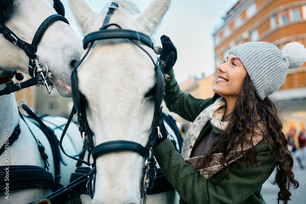 Young woman petting white horses during winter day in city.