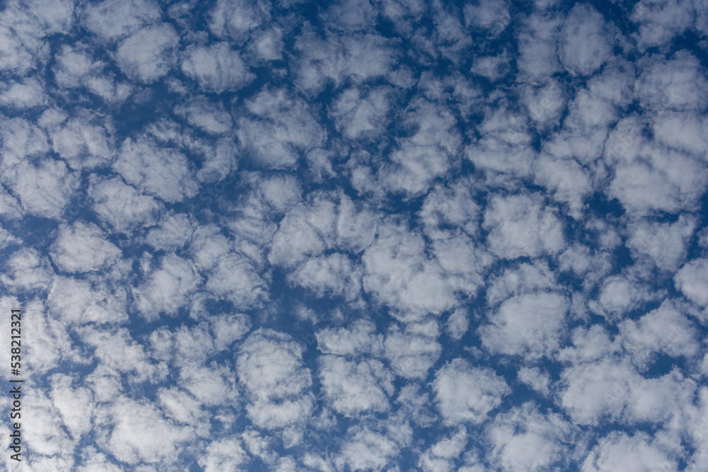 White fluffy clouds on a summer blue sky in cartoon style for background or wallpaper design. The background is white of round clouds in a blue sky. White fluffy clouds on a summer blue sky in cartoon style for background or wallpaper design. The background is white of round clouds in a blue sky.