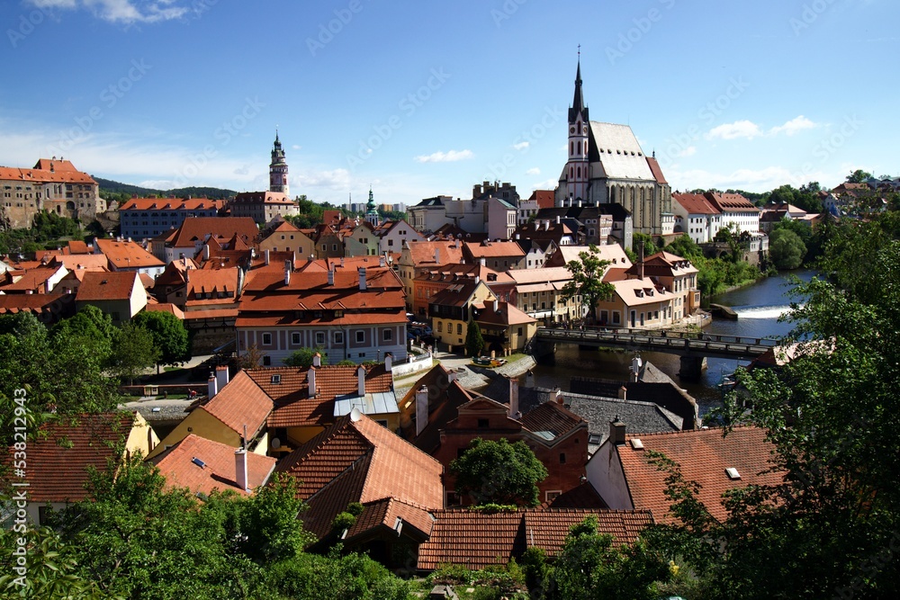 overview over Pesky Krumlov with Moldau River bridge, church and historic houses, blue sky sunny day few white clouds
