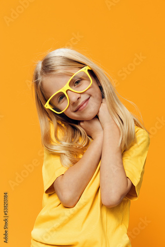 a cute, funny girl, of school age, stands on a yellow background in a yellow T-shirt in yellow glasses, posing funny. Horizontal studio photography with blank space for advertising mockup