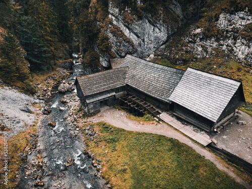 Photo of a beautiful wooden cabin with river in the forest from above - Mlyny Oblazy (Slovakia) - taken by drone. Old wooden mill with rocks on background in autumn time. - aerial photography.