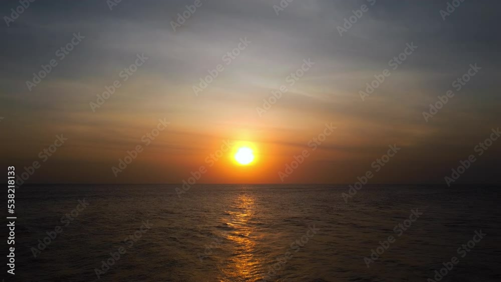 A view from a drone flying over the sea with waves and a view of the fiery sunset above the water
