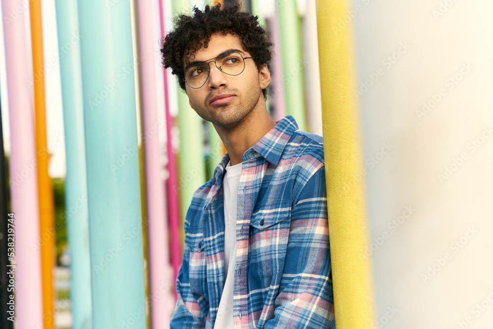 Young curly hair middle eastern man wearing eyeglasses looking away standing on urban street Young curly hair middle eastern man wearing eyeglasses looking away standing on urban street
