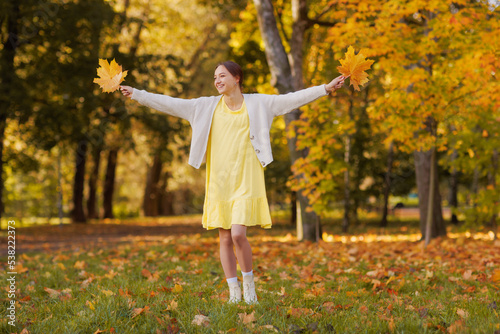 girl in yellow clothes in autumn park rejoices in autumn holding yellow leaves in her hands, warm autumn concept