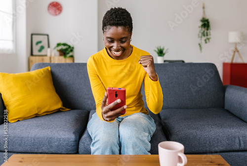 Excited young african woman celebrating online achievement success holding mobile phone - Happy female using cellphone app reading good news or lottery gambling win - Winner and victory concept