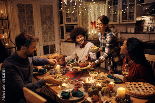 Happy woman bringing food at table while hosting Thanksgiving dinner.