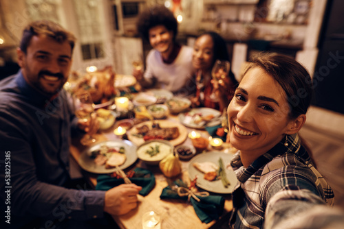 Young happy woman taking selfie with her friends during Thanksgiving dinner party.