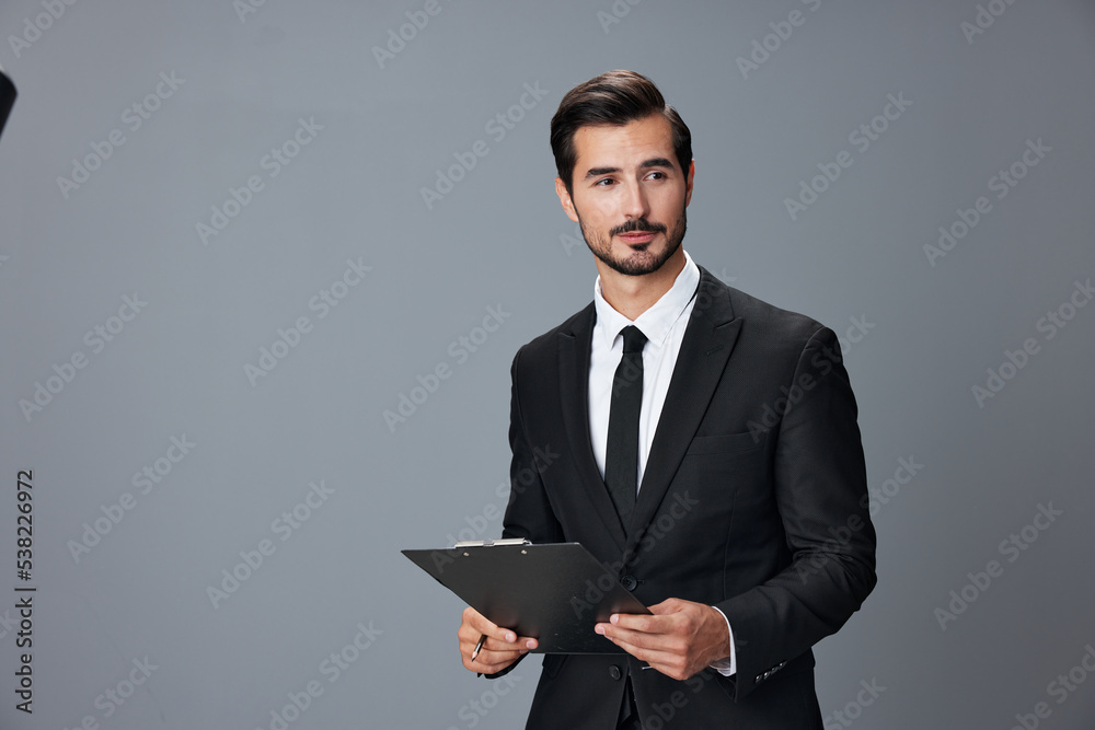 Portrait of a business man in a stylish suit smile with teeth hands up handsome face on gray isolated background with tablet in hand. Business concept young businessman startup copy space. Portrait of a business man in a stylish suit smile with teeth hands up handsome face on gray isolated background with tablet in hand. Business concept young businessman startup copy space.