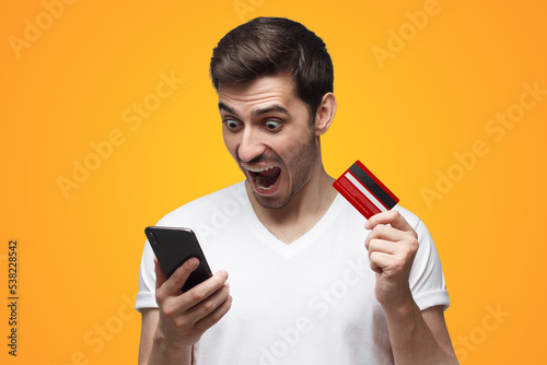 Angry man, holding credit card and phone, shouting having problem with bank account or money