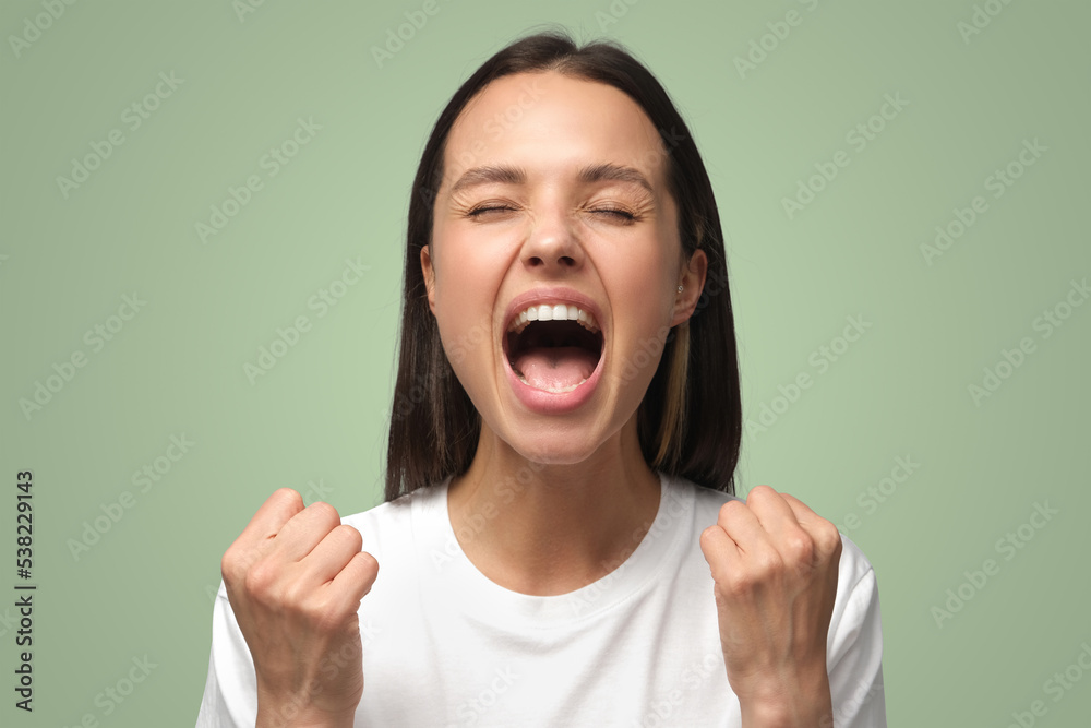 Attractive woman shouting with closed eyes while her team win, raised both fists in victory gesture Attractive woman shouting with closed eyes while her team win, raised both fists in victory gesture