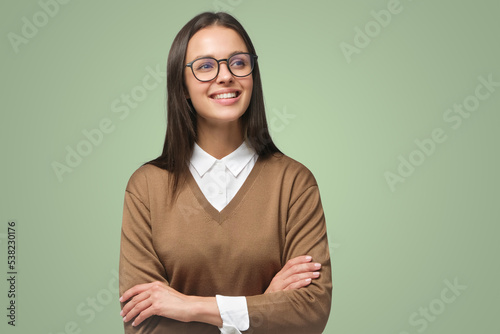 Smiling female in brown sweater standing with crossed arms looking aside, isolated on green