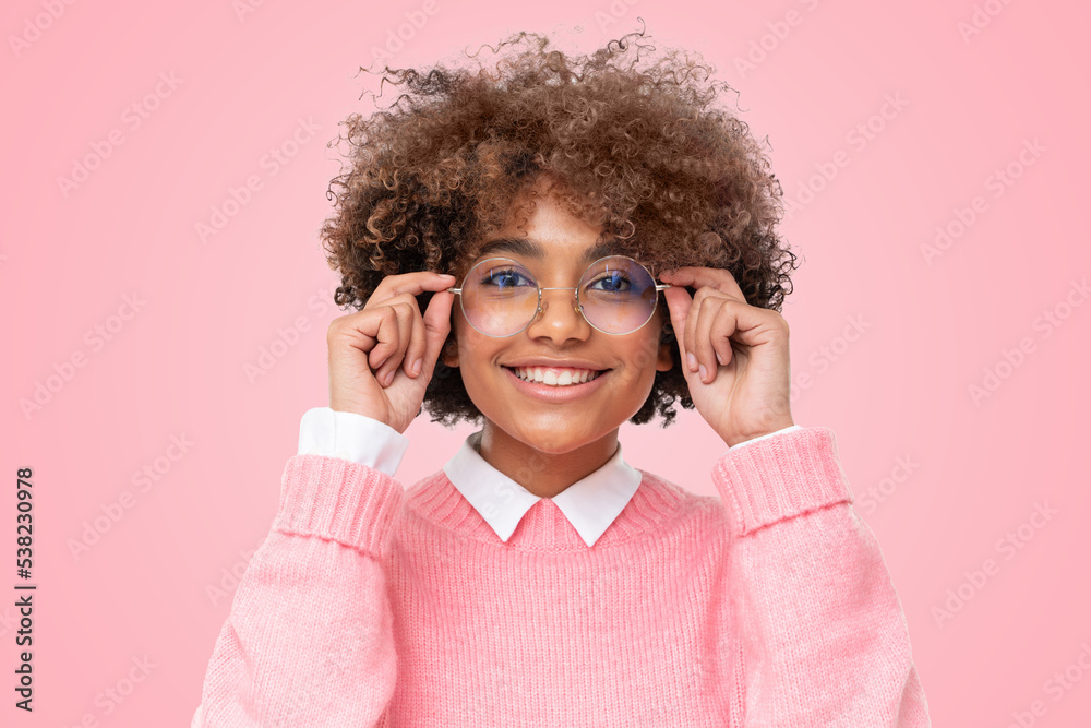 Smiling african teen girl holding eyeglasses with both hands, looking at camera on pink background Smiling african teen girl holding eyeglasses with both hands, looking at camera on pink background