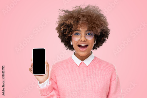 Surprised african girl excited by ads, showing blank phone screen with copy space, isolated on pink