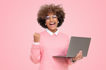 Excited young girl winner with laptop isolated on pink background