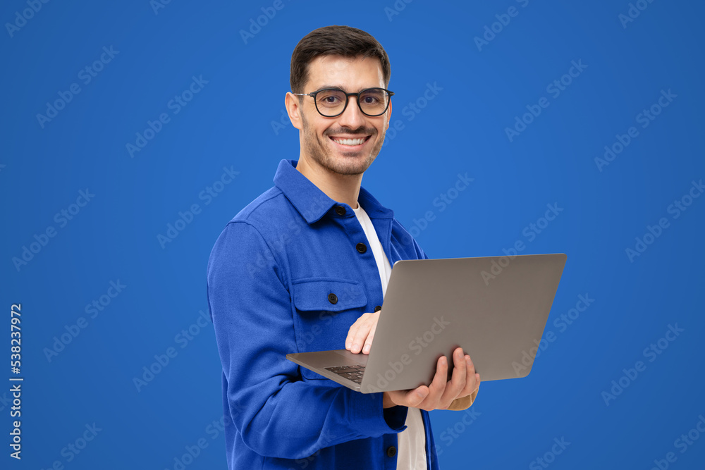 Portrait of modern business man standing in casual blue shirt, holding laptop and looking at camera Portrait of modern business man standing in casual blue shirt, holding laptop and looking at camera