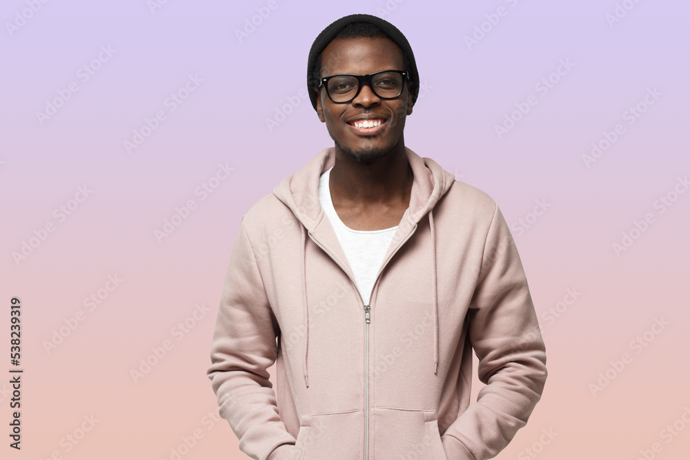 Portrait of smiling handsome african american guy in pink hoodie standing isolated on purple Portrait of smiling handsome african american guy in pink hoodie standing isolated on purple