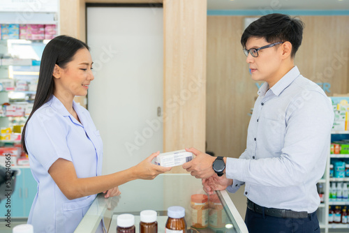 Attractive Asian woman pharmacist medication recommendation about medicine, drugs and supplements to male patient customer in modern drugstore. Medical pharmacy and healthcare providers concept.