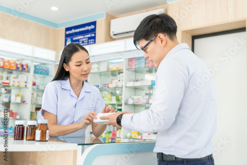 Attractive Asian woman pharmacist medication recommendation about medicine, drugs and supplements to male patient customer in modern drugstore. Medical pharmacy and healthcare providers concept.