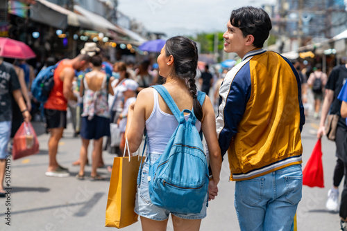Attractive Asian couple enjoy and fun outdoor lifestyle shopping at street market while travel on summer holiday vacation. Happy man and woman couple holding shopping bag walking at weekend market