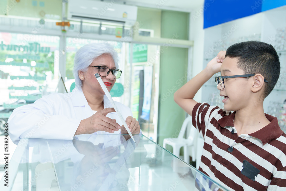 Middle-aged ophthalmologist examining young boy and giving eye consultation to Asian boy Middle-aged ophthalmologist examining young boy and giving eye consultation to Asian boy