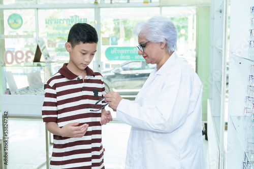 Middle-aged ophthalmologist examining young boy and giving eye consultation to Asian boy