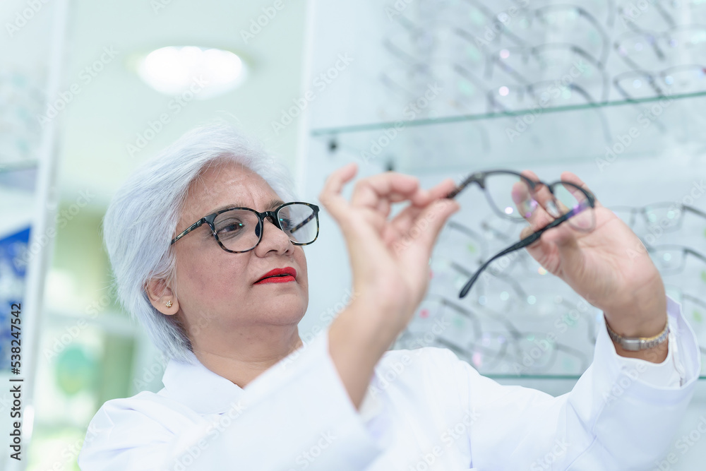 Middle aged ophthalmologist holding eyeglasses and examining them, focus on eyeglasses, close-up Middle aged ophthalmologist holding eyeglasses and examining them, focus on eyeglasses, close-up