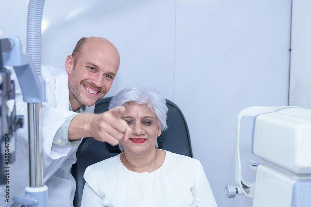 Obraz premium Attractive male ophthalmologist is checking eye vision of middle aged woman in modern clinic, doctors and ophthalmology clinic patients.