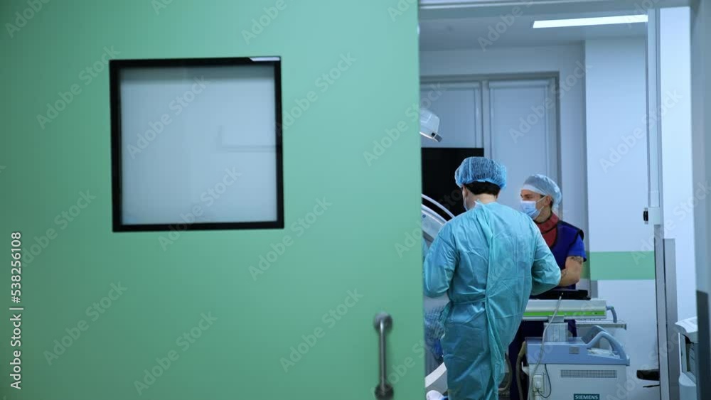 Half-opened door to a surgical theatre. Doctors working and walking in the operational room. Modern healthcare concept. Half-opened door to a surgical theatre. Doctors working and walking in the operational room. Modern healthcare concept.