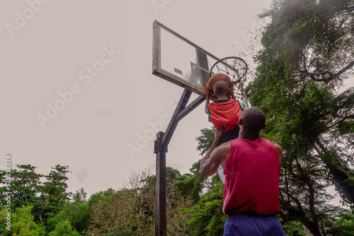 Father lifting son up to make a basket at basketball court