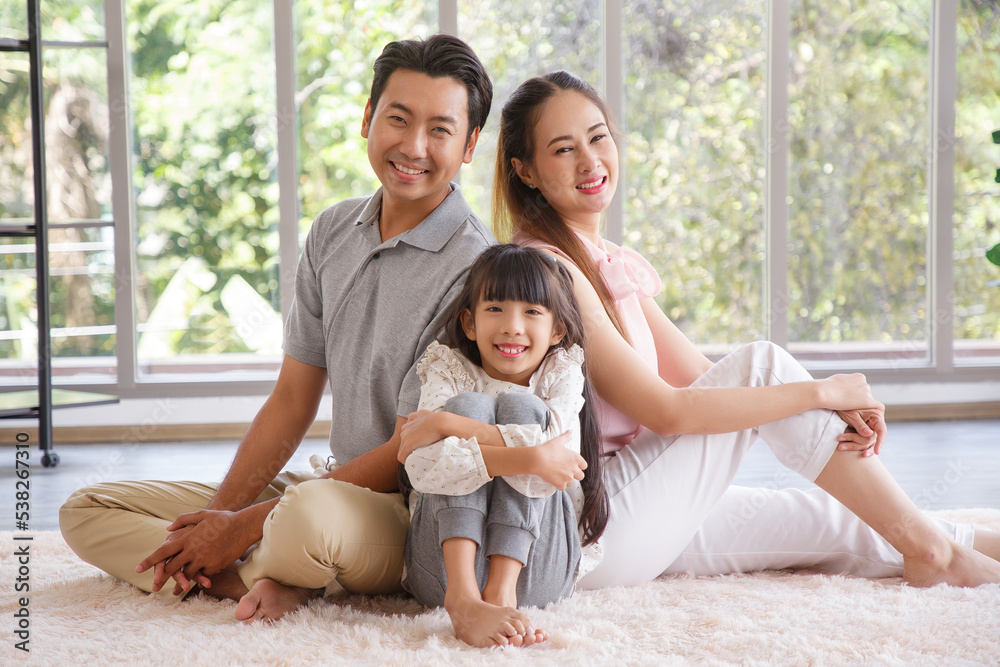 Portrait of a happy young family. Mom; dad and daughter look at the camera and smile. The faces of Asian parents and their child in living room. Family funning in living room.