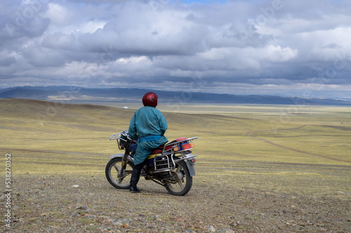 Mongolian on a motorcycle on a hill looks at the steppe