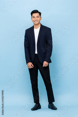 Young handsome southeast Asian man wearing semi-formal suit smiling and looking at camera in blue color studio isolated background