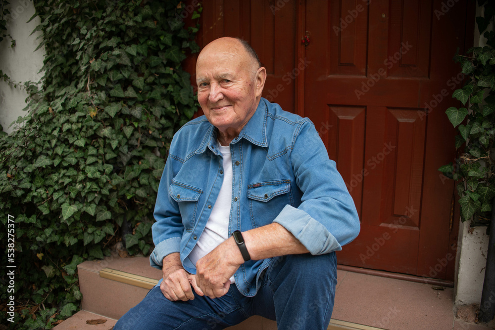 Portrait of an elderly smiling man sitting on the stairs against the background of green leaves. High quality photo. The concept of adulthood.