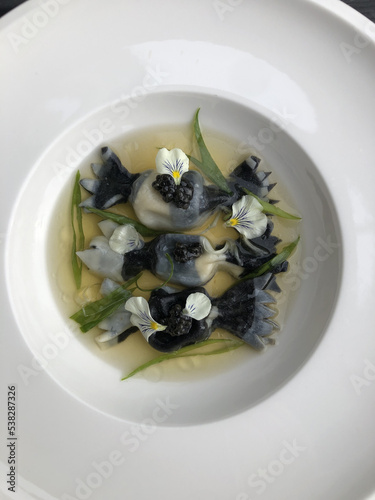 Squid ink gyozas in the shape of caramelle pasta with awase dashi, caviar, scallions, and orange-infused oil