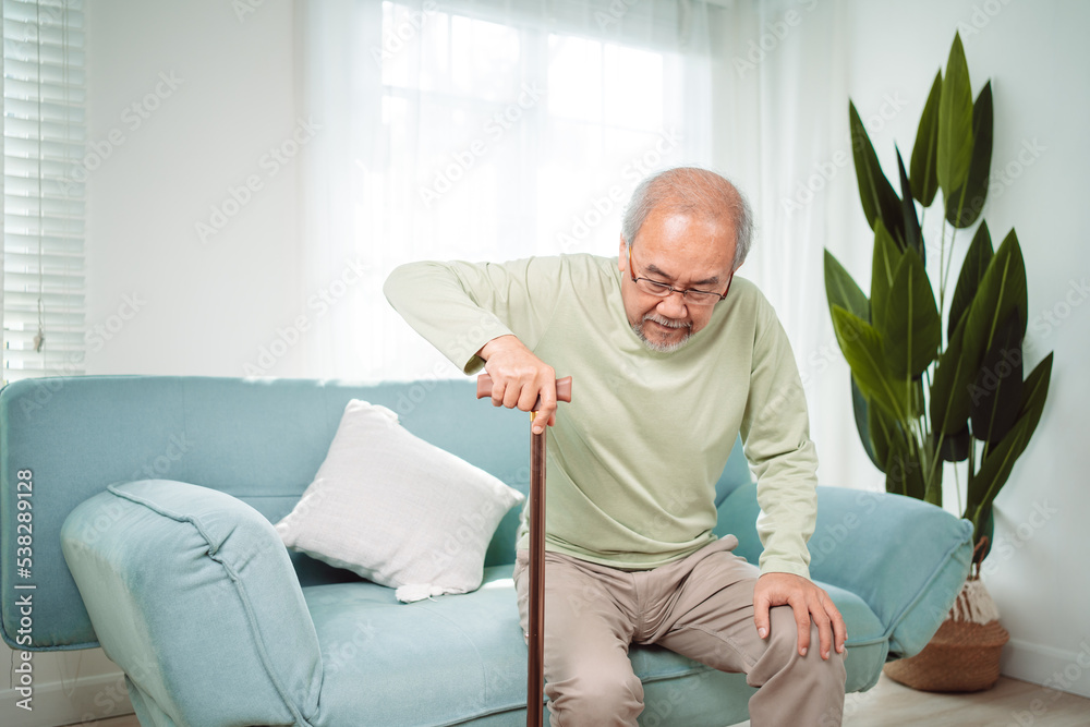Asian Senior elderly old man disabled patient walking slowly his use walker or cane in living room at home. Feeling painful and suffering from knee pain. Healthcare medical and insurance concept. Asian Senior elderly old man disabled patient walking slowly his use walker or cane in living room at home. Feeling painful and suffering from knee pain. Healthcare medical and insurance concept.