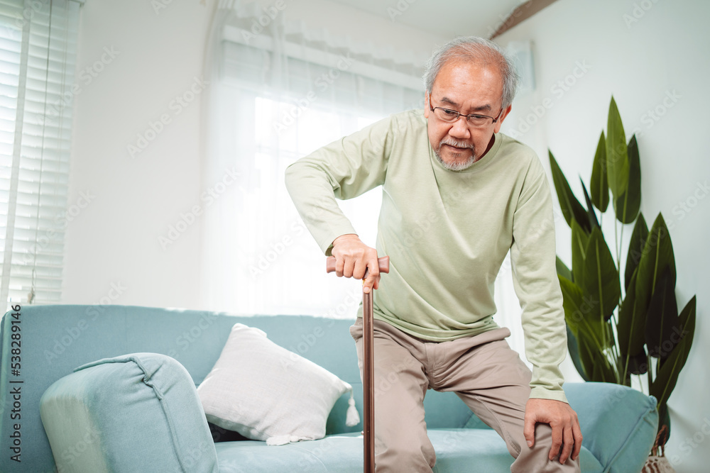 Asian Senior elderly old man disabled patient walking slowly his use walker or cane in living room at home. Feeling painful and suffering from knee pain. Healthcare medical and insurance concept.