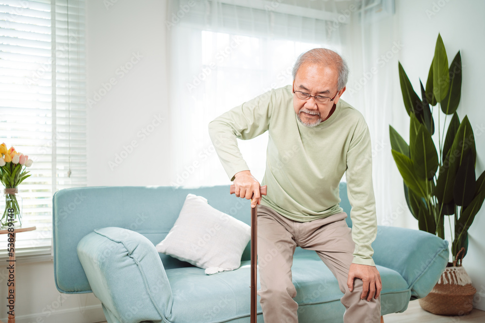 Asian Senior elderly old man disabled patient walking slowly his use walker or cane in living room at home. Feeling painful and suffering from knee pain. Healthcare medical and insurance concept. Asian Senior elderly old man disabled patient walking slowly his use walker or cane in living room at home. Feeling painful and suffering from knee pain. Healthcare medical and insurance concept.