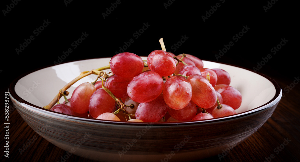 A bunch of ripe red grapes lies in a plate, side view. Beautiful red grapes. A bunch of ripe red grapes lies in a plate, side view. Beautiful red grapes.