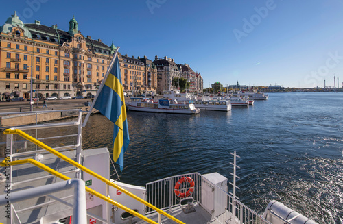 Stern view of a commuting boat in the bay Nybroviken over a pier with boats apartment and office houses a sunny a color full autumn day in Stockholm photo