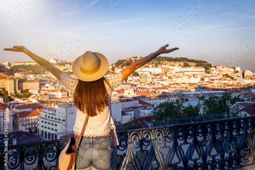 A happy tourist woman overlooks the colorful old town Alfama of Lisbon city, Portugal, and castle Sao Jorge during sunset time