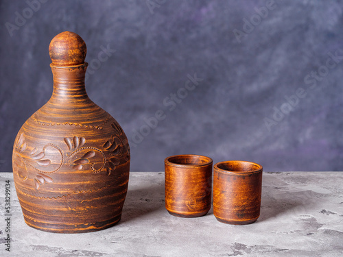 Clay pitcher and two ceramic shot glasses on a rustic background photo