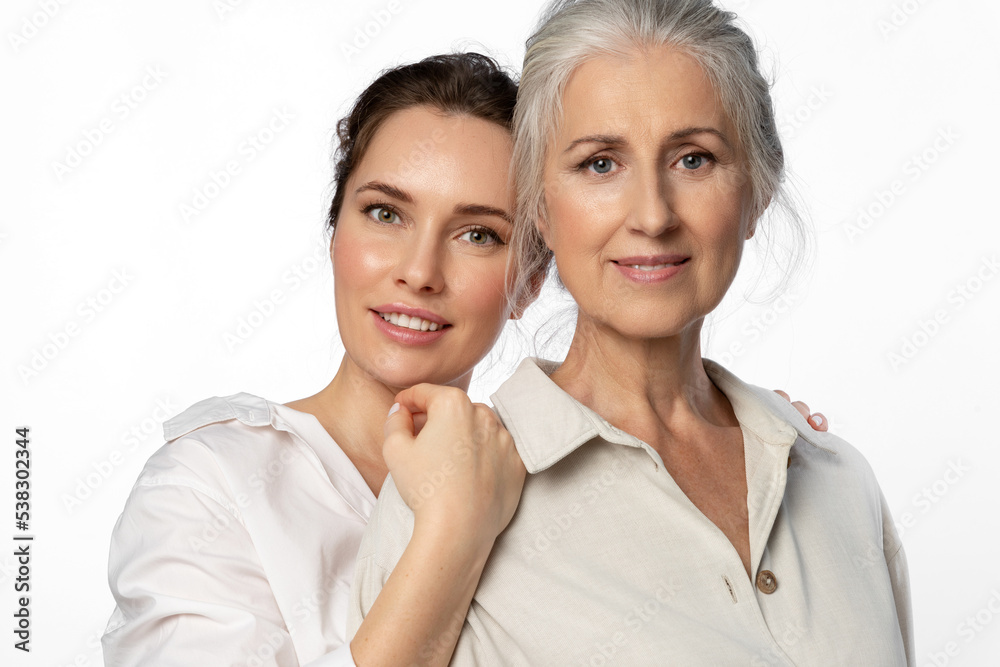 Daughter and her elderly mother, two beautiful women of different generations on a white background looking into the camera. Daughter and her elderly mother, two beautiful women of different generations on a white background looking into the camera.