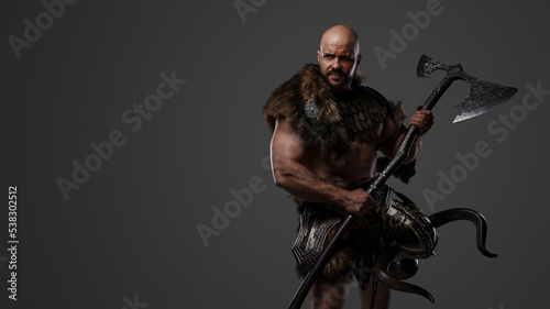 Portrait of nordic warrior with muscular build dressed in armor holding axe.