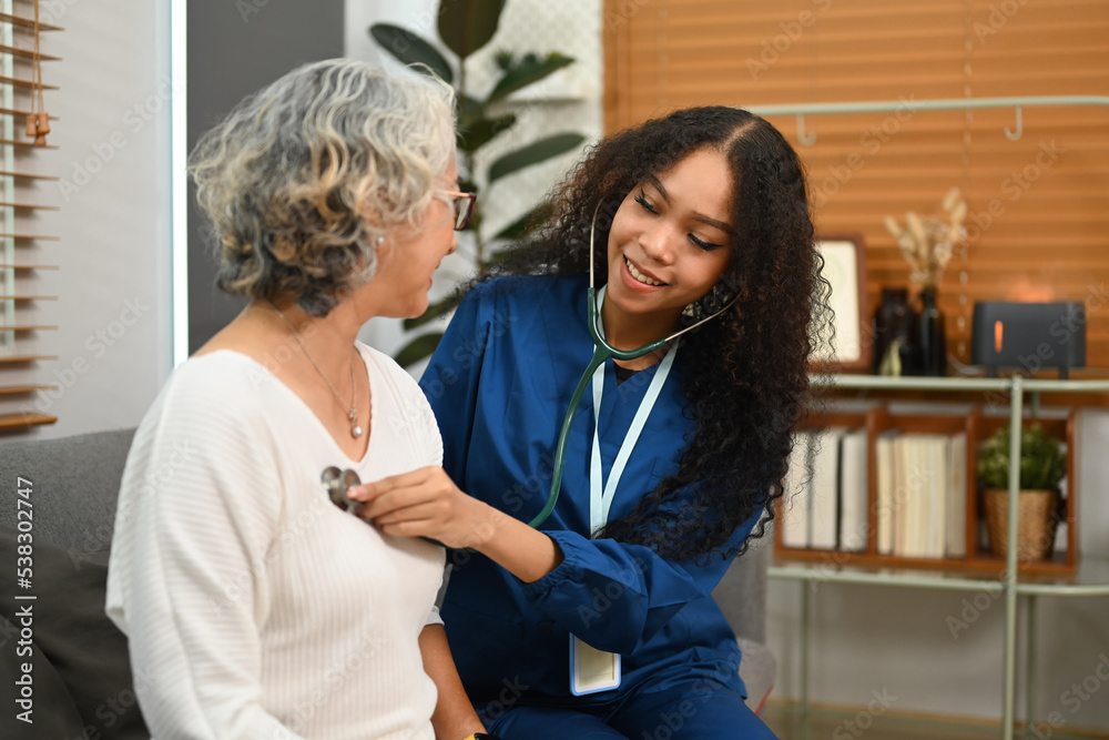 Obraz premium Carrying female doctor holding stethoscope checking heartbeat during home care visit. Elderly healthcare concept