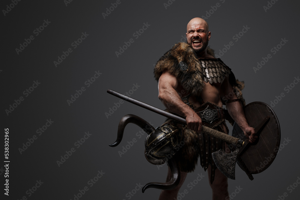 Portrait of violent barbaric viking dressed in armor and fur holding shield and axe. Portrait of violent barbaric viking dressed in armor and fur holding shield and axe.