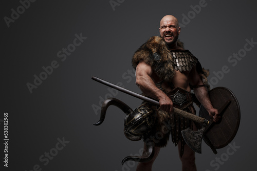 Portrait of violent barbaric viking dressed in armor and fur holding shield and axe.