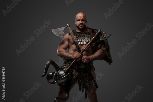 Shot of bloodthirstly viking from past dressed in armor and fur against grey background.